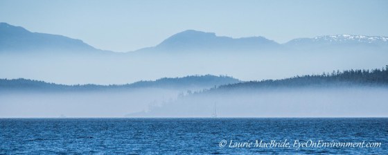 Blue sea and skies with layers of fog and boats in distance