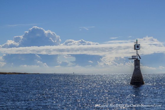 Navigational light with bright sun on water and clouds