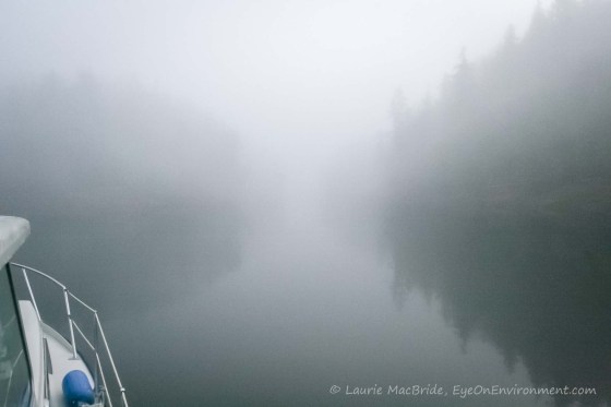 Foredeck of boat with islands nearby, barely visible through the fog.